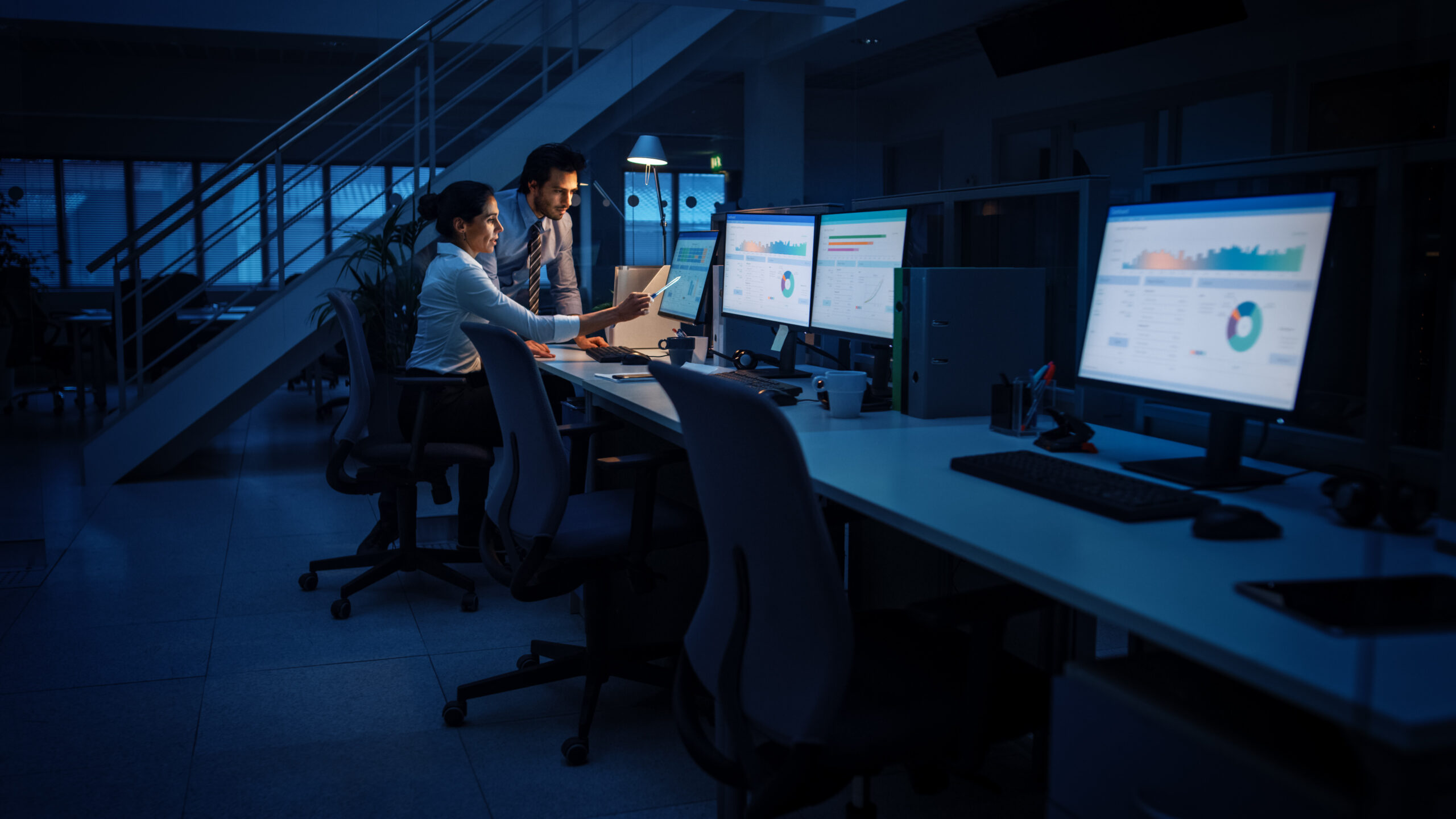 Late at Night In Modern Office: Businessman and Businesswoman Work on Desktop Computer, Having Discussion, Finding Problem Solution, Finishing Project. Successful Dedicated Responsible Office Workers